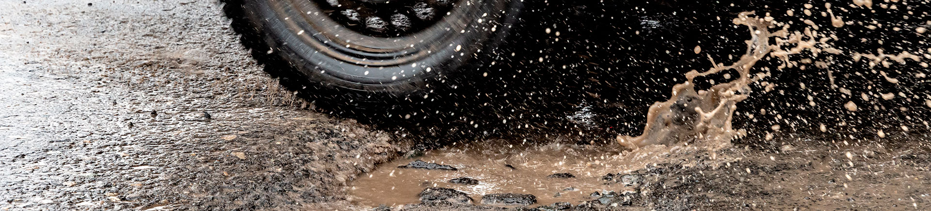 car driving on asphalt road with potholes filled with rainwater