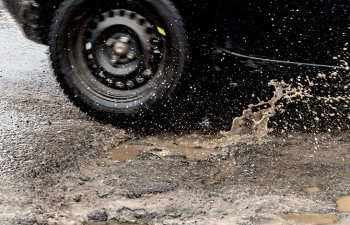 car driving on asphalt road with potholes filled with rainwater