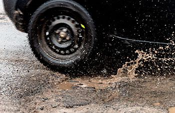 car driving on asphalt road with potholes filled with rainwater