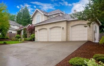 large beige houses with three car garage and large wet concrete driveway under a blue sky